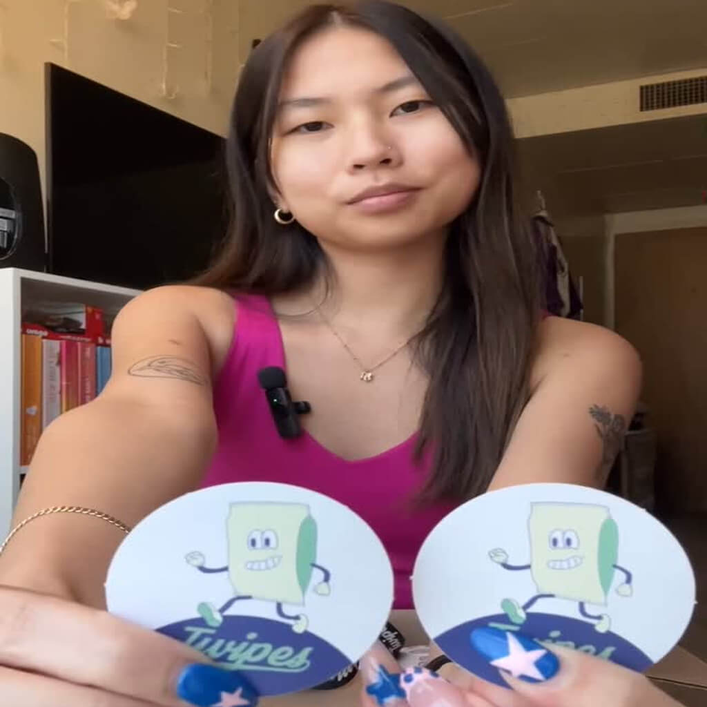 Social media post of a woman holding two stickers of a cartoon of a pack of wet wipes